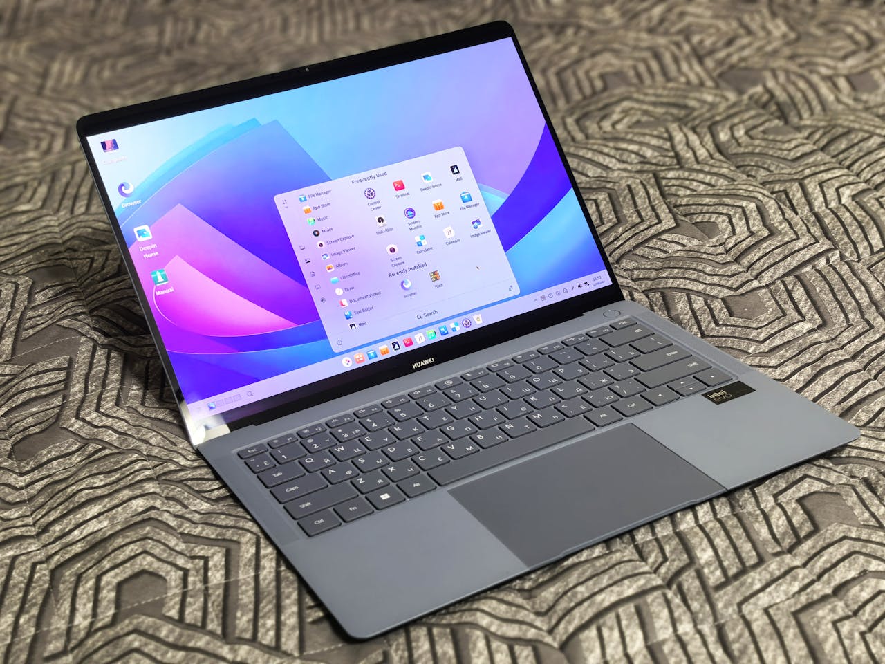 A sleek modern laptop with an open application menu on a patterned surface.